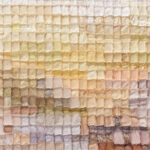Close-up of a pastel patchwork quilt made of small square fabric patches in pale yellows, creams, and pinks, with visible stitching.