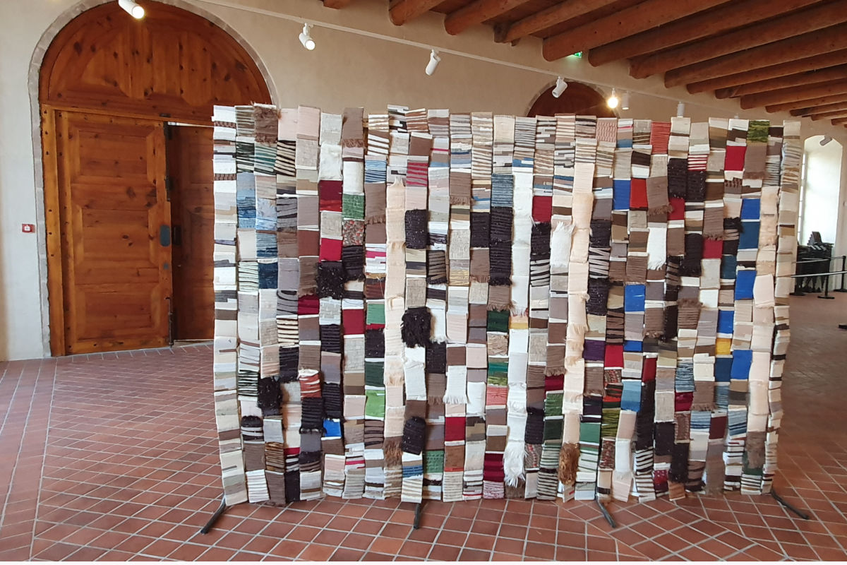FITE 2020 Regards textiles sur les tapisseries de la Chaise-Dieu ©Thomas Leveugle Panel covered with many colorful fabric swatches arranged in vertical columns in a gallery space.