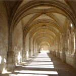 Sunlit stone cloister: a long vaulted arcade with repeating arches along a corridor.