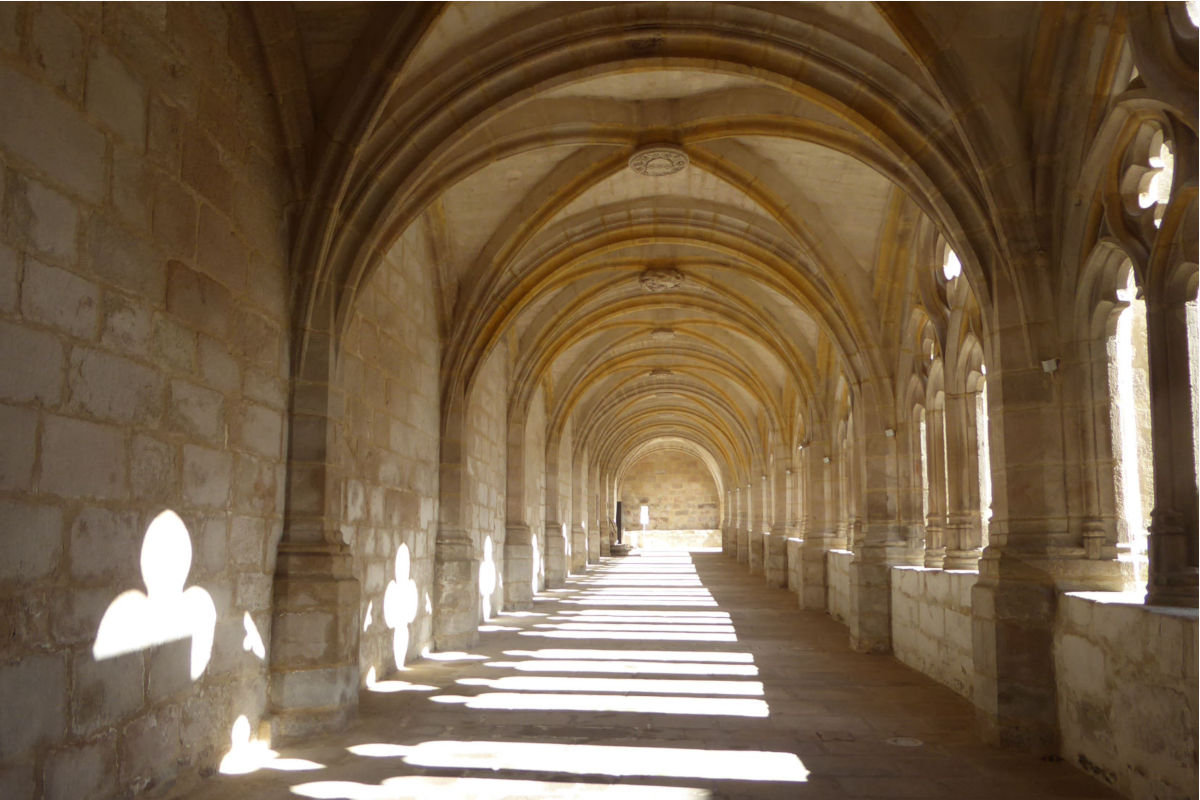 Sunlit stone cloister: a long vaulted arcade with repeating arches along a corridor.