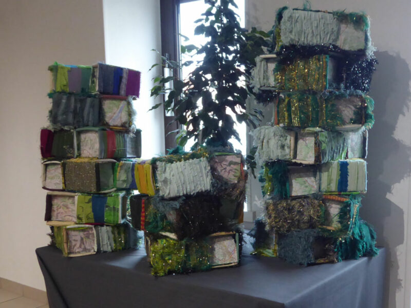 Colorful fabric-wrapped boxes stacked into two towers on a table, with a plant in the background.