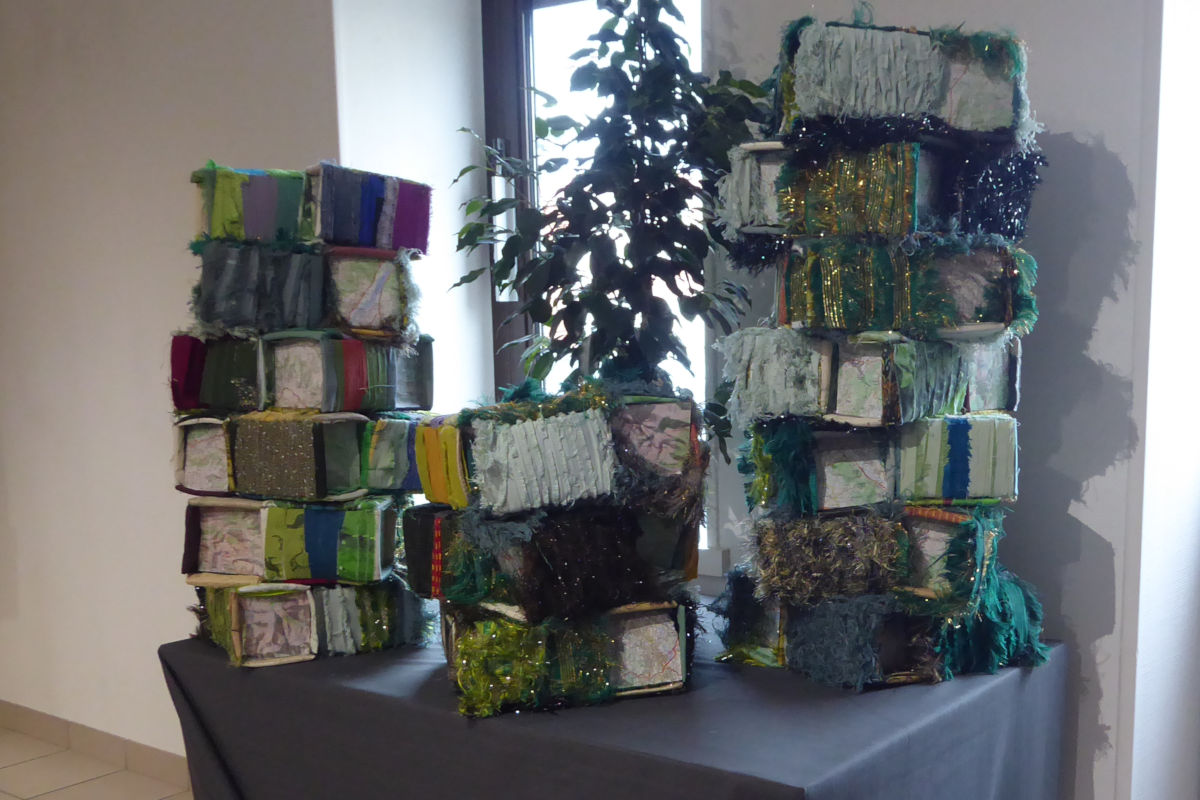 Colorful fabric-wrapped boxes stacked into two towers on a table, with a plant in the background.