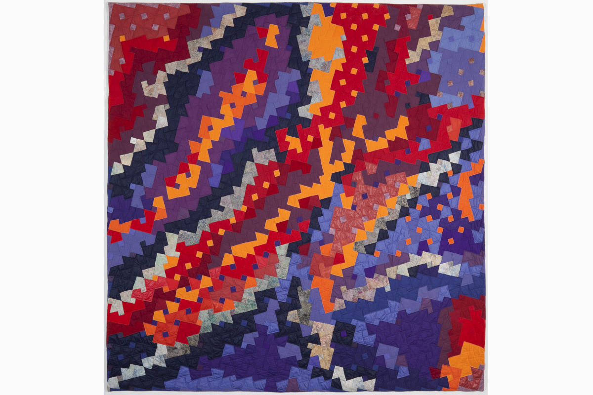 Sabine Cibert Abyss ©Philippe-Liev Pourcelot Colorful geometric quilt with diagonal bands of interlocking triangle shapes in red, orange, purple, and blue.