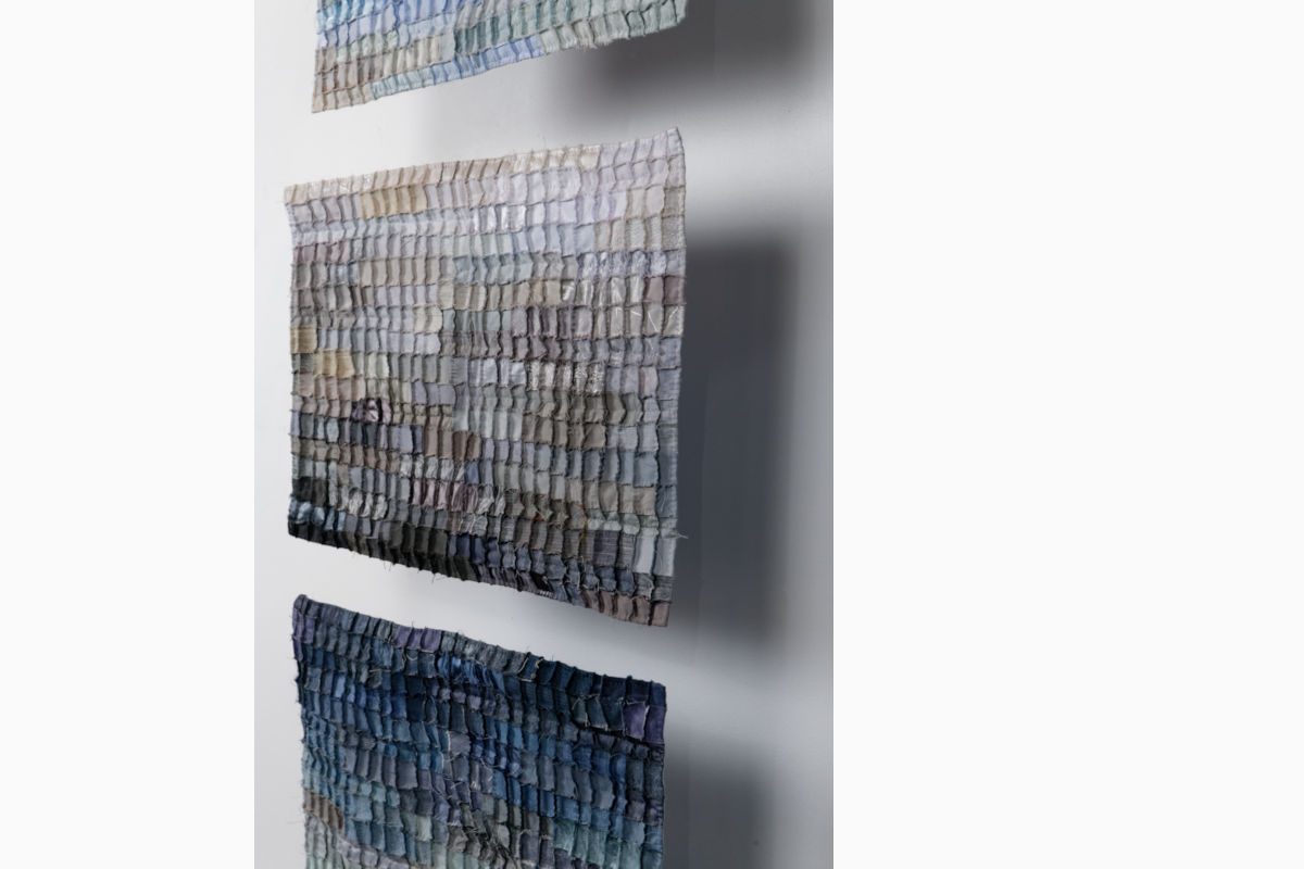 Three wall-mounted textile mosaic panels made of small fabric squares in blue-gray-beige tones, arranged vertically on a white wall.]