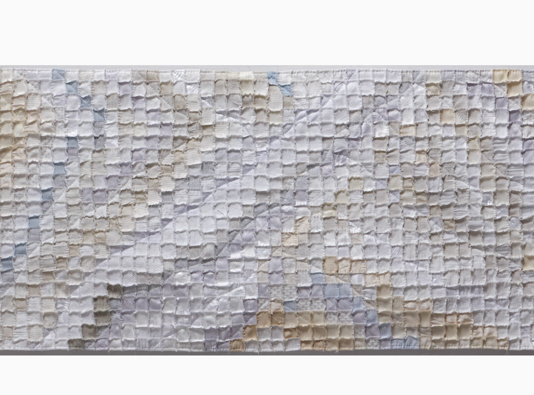 Abstract quilted textile wall hanging made of small square patches in cream, beige, and pale gray tones.