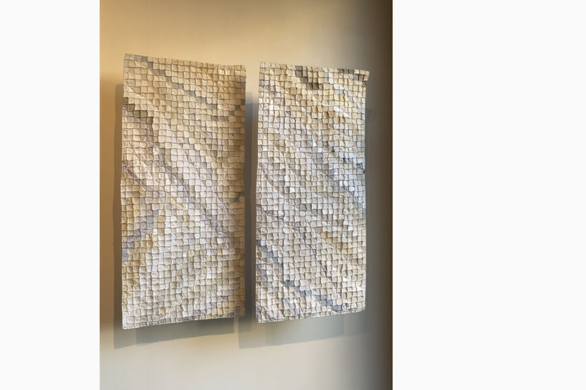 Two vertical mosaic panels made of small square tiles in beige and cream tones mounted on a wall with subtle shadows below.