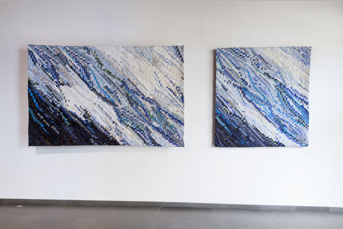 Sabine Cibert Eau vive 1 et 3 exposition ©Philippe-Liev Pourcelot Two abstract mosaic paintings on a white gallery wall, featuring diagonal blue and white patterns; a larger left piece and a smaller right piece side by side.