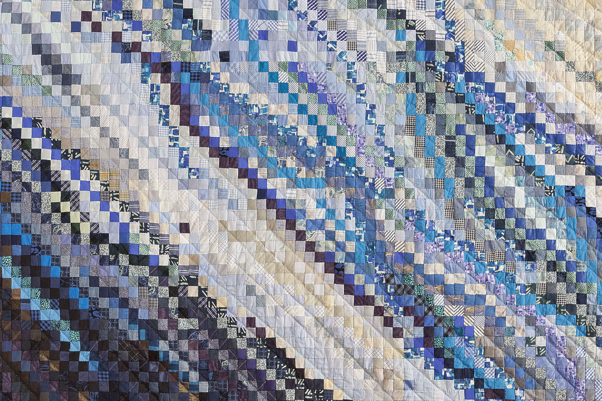 Sabine Cibert Eau vive1 détail ©Philippe-Liev Pourcelot Patchwork quilt made of small blue, purple, and cream squares arranged in diagonal wave patterns across the quilt.