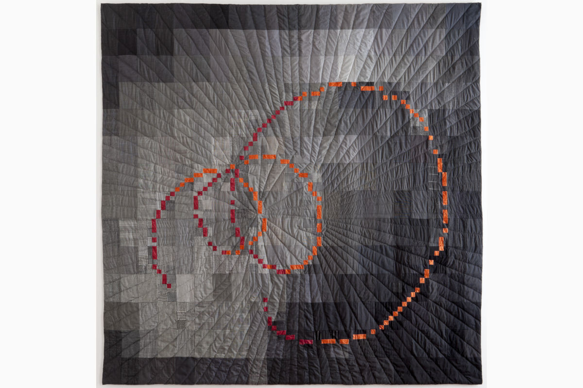 Sabine-Cibert-Espace-temps 1 ©Philippe-Liev Pourcelot Abstract quilt with a bright orange dotted spiral over a grayscale patchwork background.