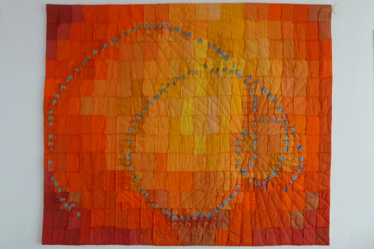 Sabine Cibert Espace-temps 7 ©Sabine Cibert Abstract quilt with a fiery orange gradient and a spiral of small blue-gray squares on a wall hanging.