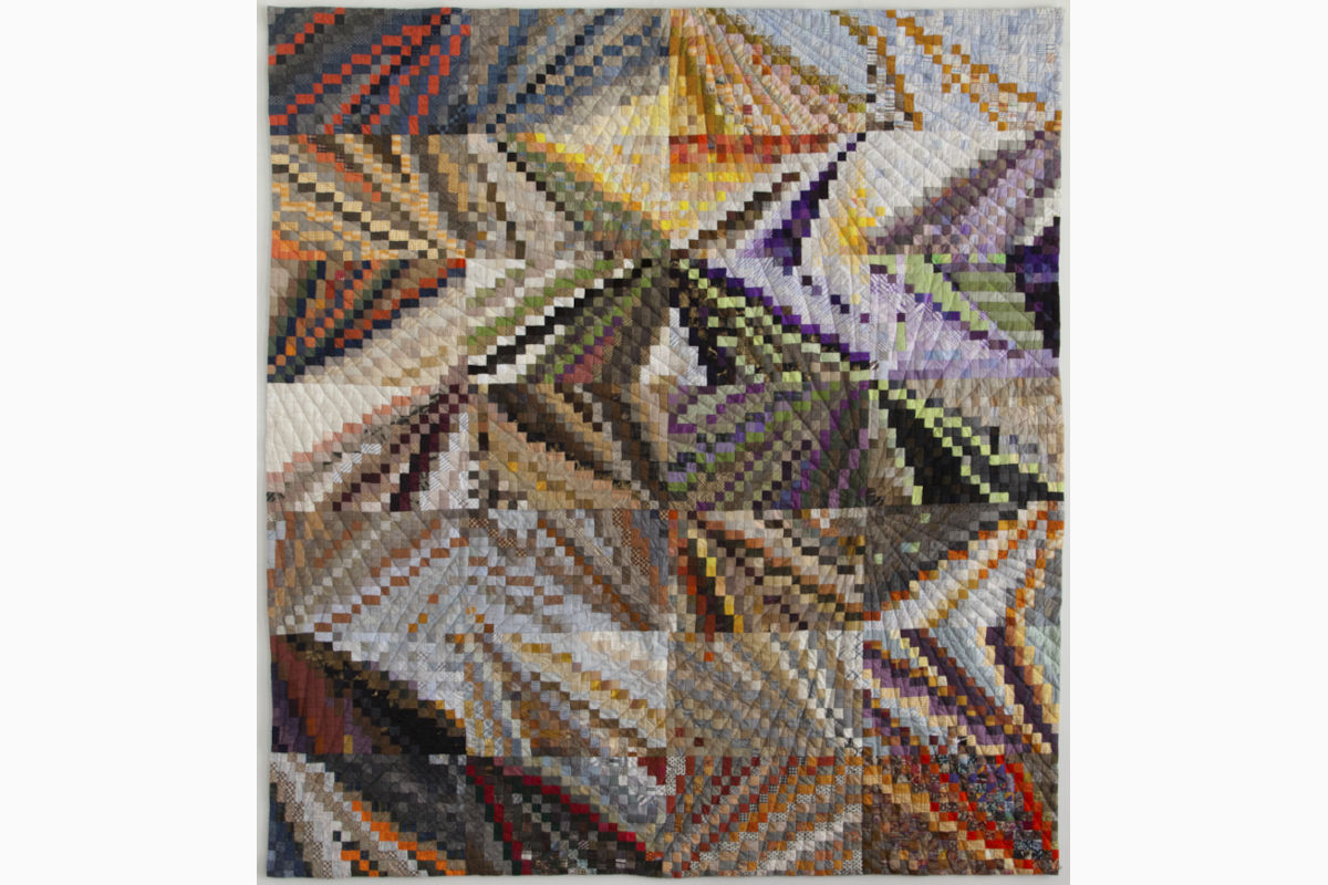 Sabine-Cibert Instants1 ©Philippe-Liev Pourcelot Colorful patchwork quilt with intricate diagonal and triangular blocks in warm and cool tones.