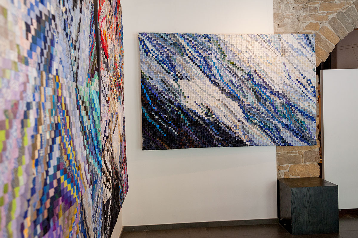 Sabine Cibert Instants 3 Instants 2 détails au fond Eau vive ©Philippe-Liev Pourcelot Large abstract quilt mosaic of blue, purple, and white squares hanging on a white wall in a gallery.