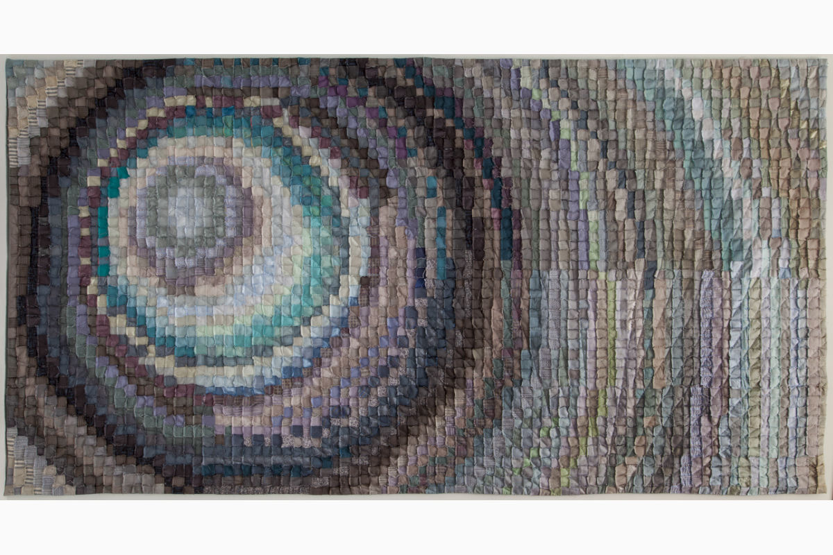 Textile wall hanging with a spiral of small fabric squares in blues, teals, and browns.
