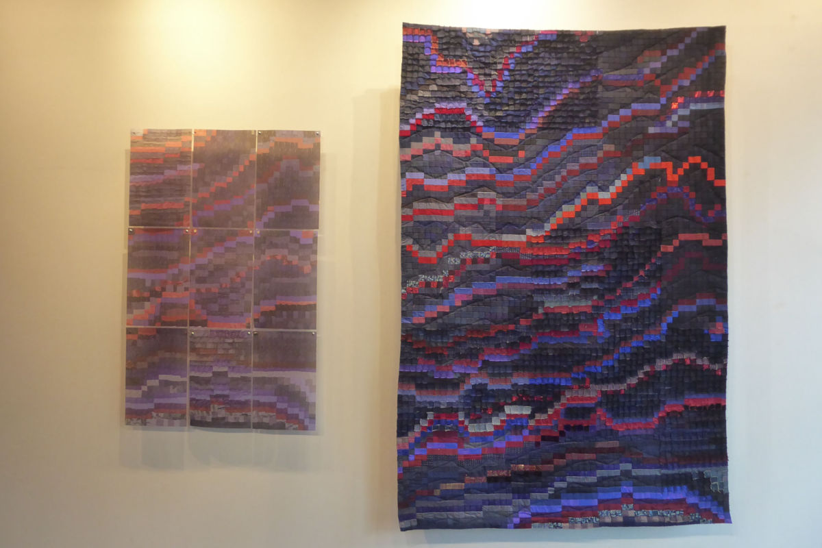 SabineCibert - Magma et son archétype ©Thomas Leveugle Two abstract textile pieces on a pale wall: a large, vertically oriented quilt with wavy red, purple, and blue blocks; beside it a smaller multi-panel piece with a similar pattern in purples and pinks.