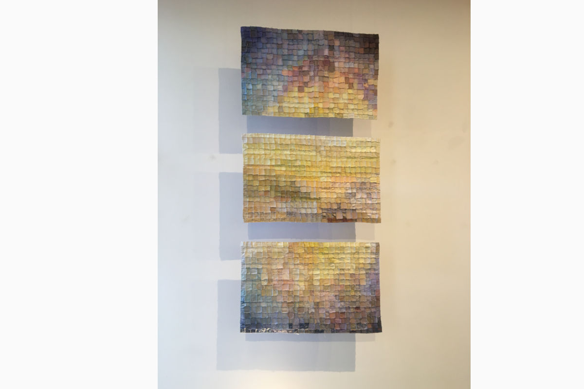 Three stacked mosaic panels on a wall, made of small square tiles in a cool-to-warm gradient.