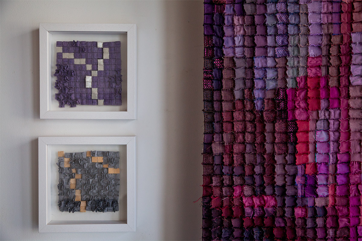 Sabine Cibert Orage 322 Orage301 Boreale295, détail ©Philippe-Liev Pourcelot Two white-framed textile art pieces mounted on a light wall, each featuring purple and gray square patches; a large multicolor patchwork textile hangs to the right.