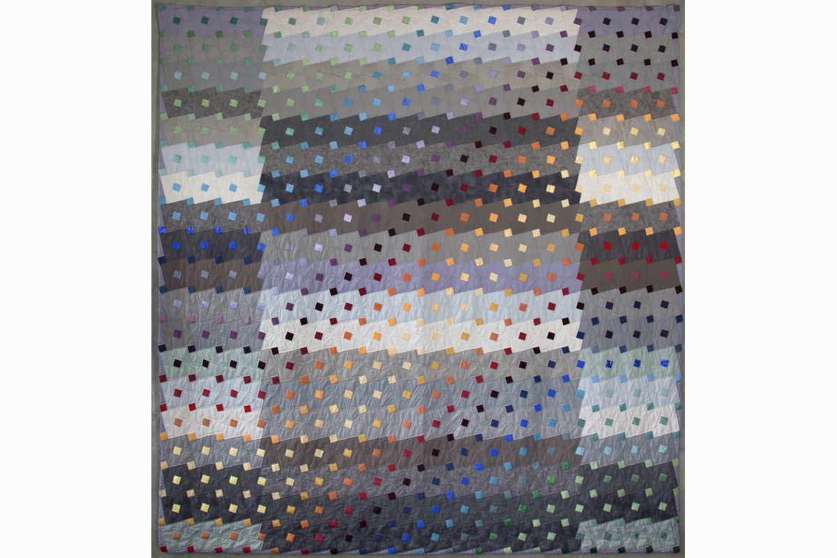 Sabine Cibert- Pluie de couleur sur Grenade ©Philippe-Liev Pourcelot Patchwork quilt with diagonal rows of small colorful squares on a muted gradient background.