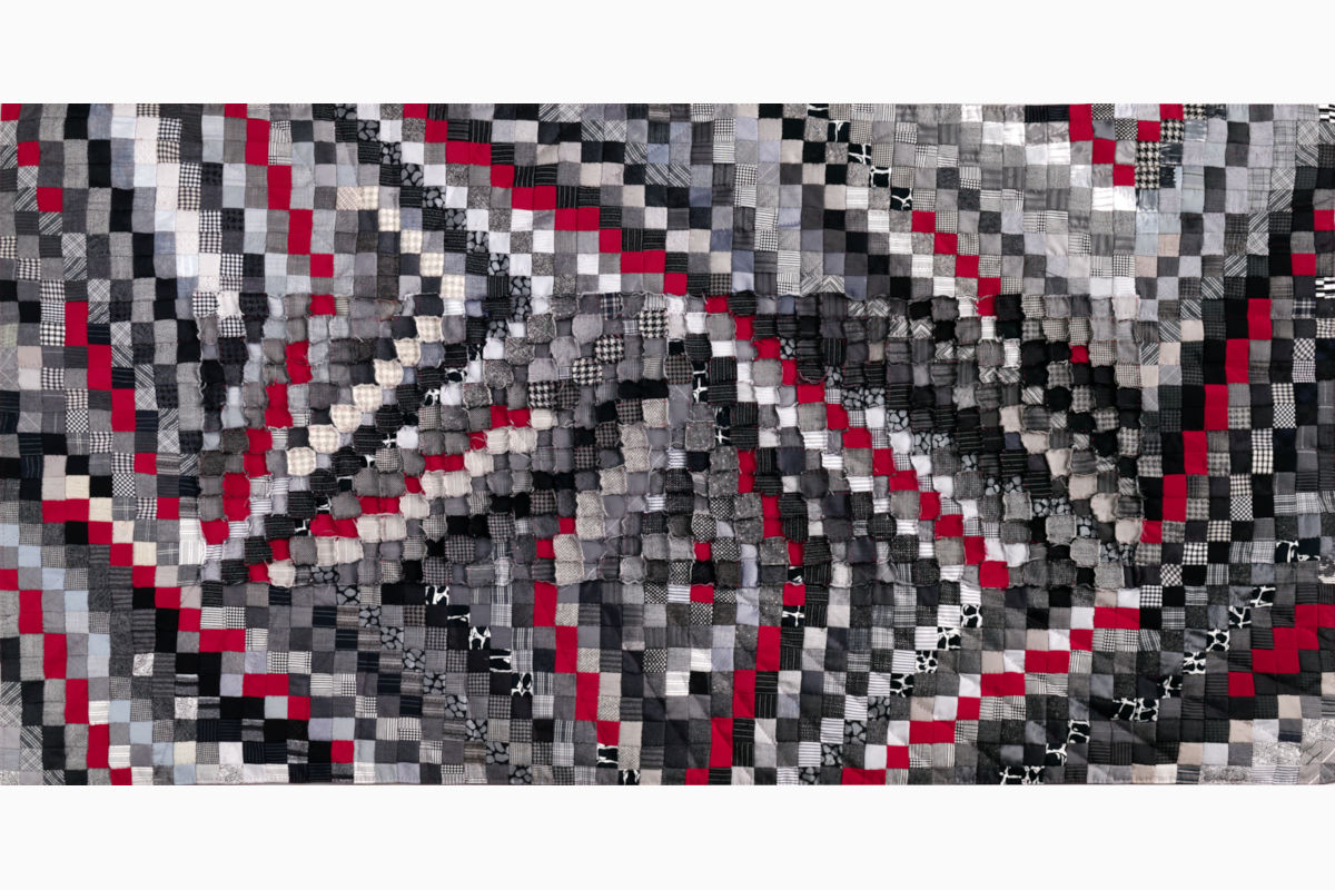 Sabine Cibert Sémagramme 217 ©Pascal Muradian Patchwork quilt made of small grayscale squares with red accents forming a swirling pattern.