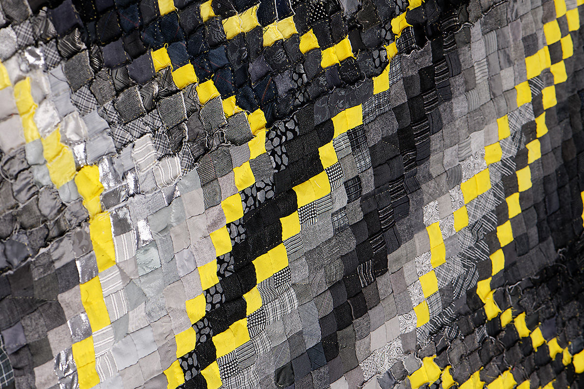 Sabine Cibert Sémagramme 218-detail ©Pascal Muradian Close-up of a patchwork quilt made from small gray, black, and yellow squares, showing textured fabric squares arranged in diagonal bands.