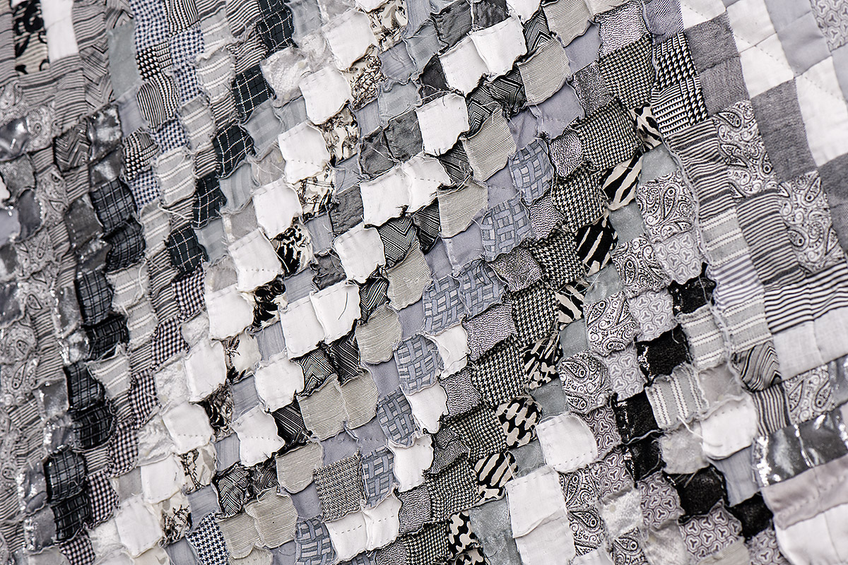 Sabine Cibert Sémagramme 219 Détail ©Pascal Muradian Close-up of a grayscale patchwork quilt made from tiny fabric squares in varying patterns and textures.
