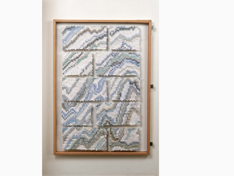 Framed wooden display with nine mosaic tile panels forming blue-gray wave patterns in white, arranged in a grid inside a light wood frame