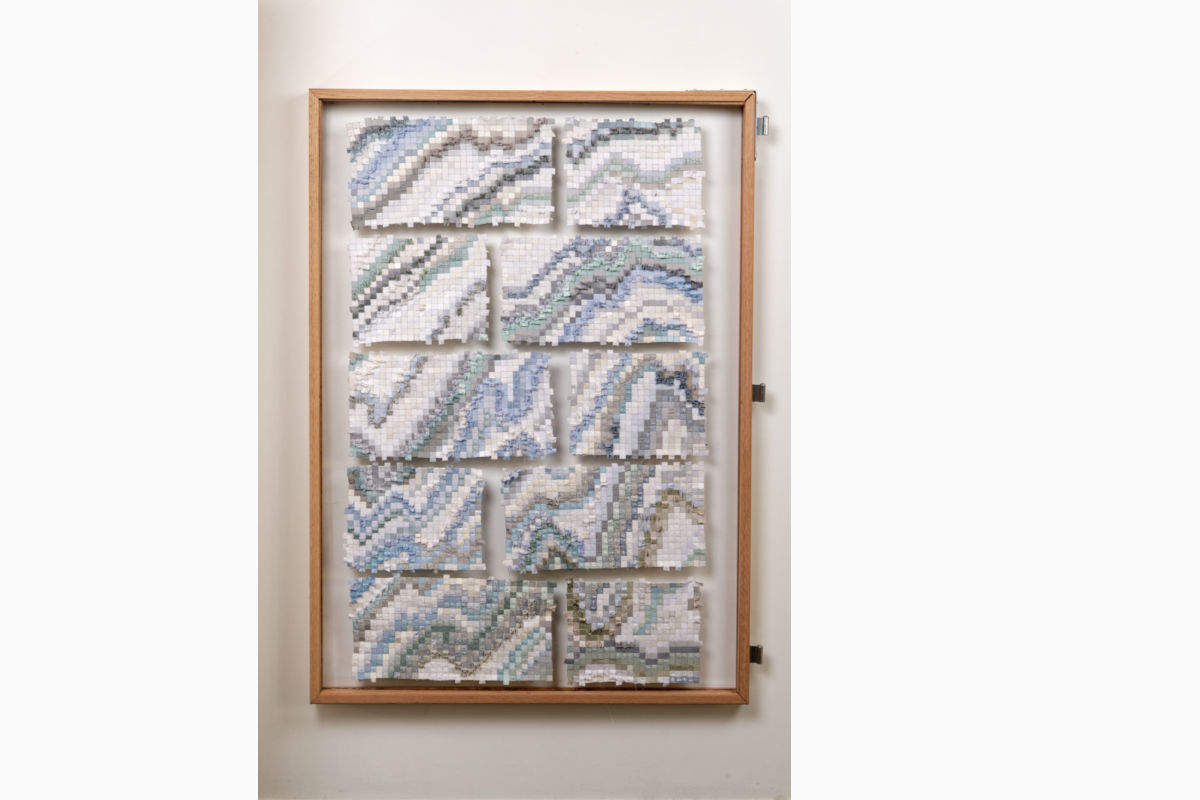 Framed wooden display with nine mosaic tile panels forming blue-gray wave patterns in white, arranged in a grid inside a light wood frame