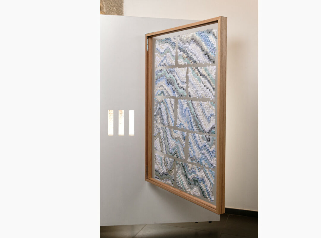 Sabine Cibert Sikuliaq face B de biais ©Pascal Muradian Wooden-framed mosaic panel with blue-gray-white pieces leaning against a light wall, an abstract wall art installation.