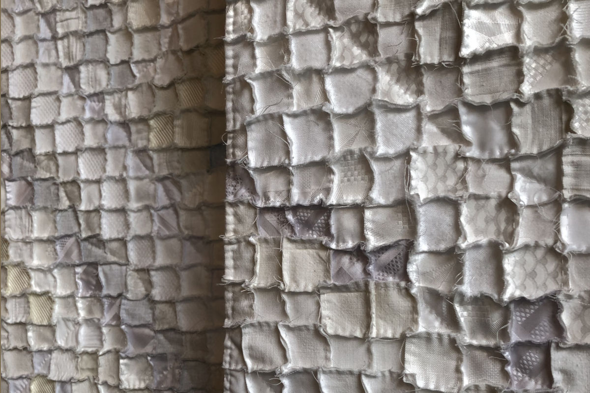 Close-up of a quilted fabric wall hanging made of small square patches in neutral beige and gray tones.