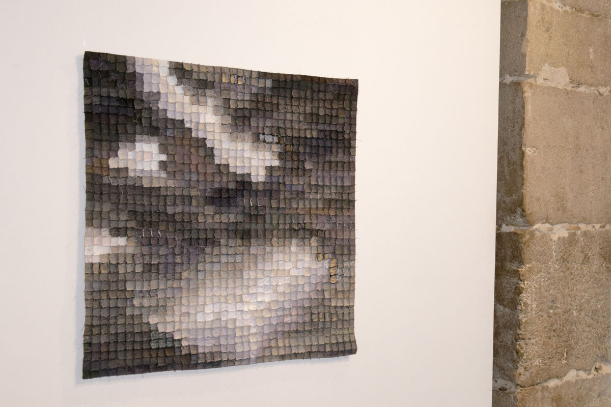 Sabine Cibert - Boréale.295 ©Pascal Muradian Grayscale mosaic square artwork made of small square tiles mounted on a white gallery wall, adjacent to a stone wall.