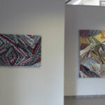 Two abstract mosaic paintings on light gray gallery walls; left piece uses grayscale tiles with red accents in a wavy, zigzag pattern, right piece uses multicolored geometric shards arranged in angular segments.