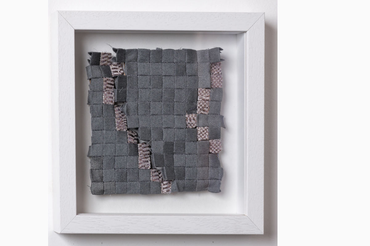 Sabine Cibert - Orage 299 ©Pascal Muradian Framed textile art: a patchwork of gray fabric squares woven together, with pink patterned strips, displayed in a white frame.